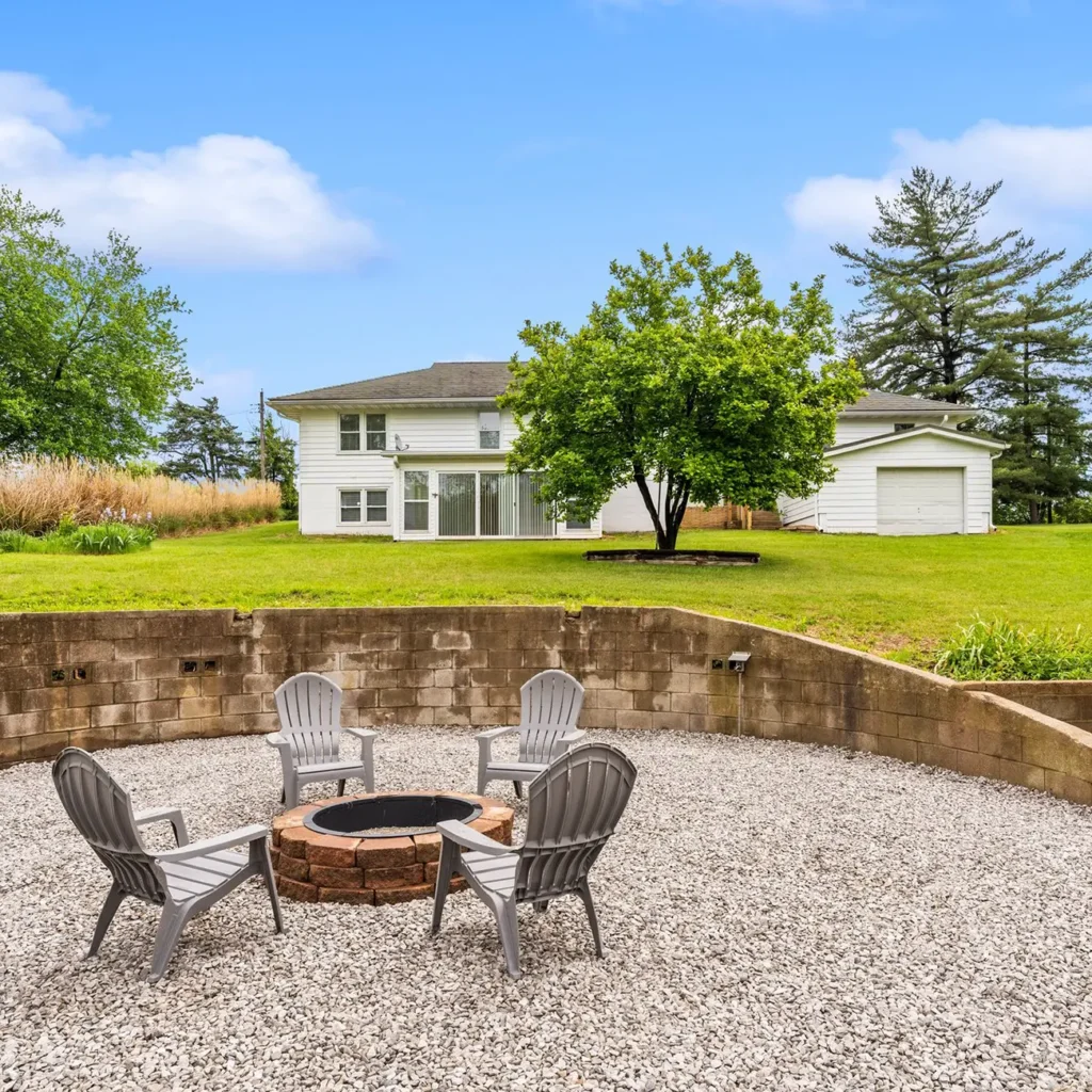 Backyard patio with fire pit seating area overlooking a white home and large green lawn