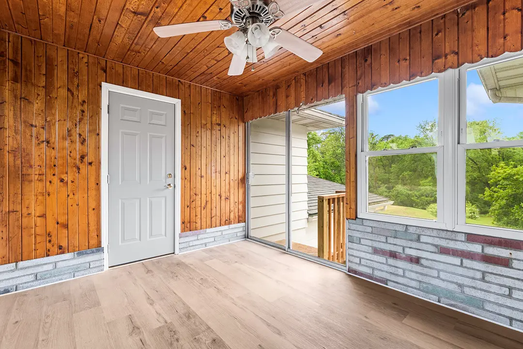 Enclosed sunroom with wood paneling, large windows, sliding glass door, and ceiling fan